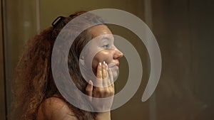 Mixed race young woman with curly hair applies make-up base