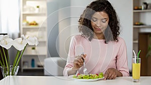 Mixed race young woman eating salad at table, healthcare and healthy dieting