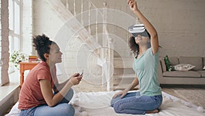 Mixed raced woman using virtual reality glasses while her friend holding digital tablet computer. Girlfriends play video