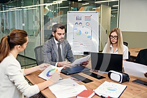 Mixed races coworkers analysing different business papers and working with computers at the tables in modern office.