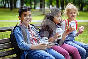 Mixed Racial Group of school kids eating lunch together on break outdoors near school. Back to school concept.