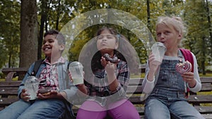 Mixed Racial Group of school kids eating lunch together on break outdoors near school. Back to school concept. Slow