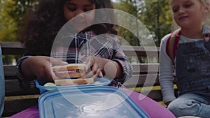 Mixed Racial Group of school kids eating lunch together on break outdoors near school. Back to school concept. Slow