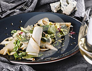 Mixed salad with pear, cheese gorgonzola and sea buckthorn sauce in a ceramic plate over grey background. Healthy vegan food,