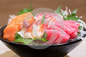 Mixed sliced fish sashimi on ice in black bowl. Sashimi Salmon Tuna Hamachi Prawn and Surf Calm set, raw fish, japanese food in