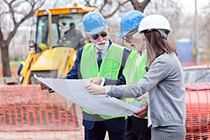 Mixed team of engineers meeting and discussing blueprints while visiting construction site site