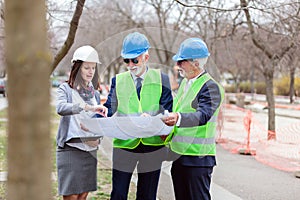 Mixed team of senior men and young female architects or business partners looking at building plans on a construction site