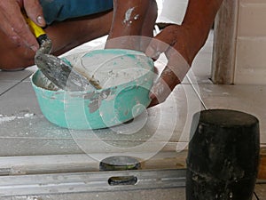 Mixed tile grout in a plastic bowl in a construction worker`s hands ready to be used for grouting ceramic tile floor - tiling wor