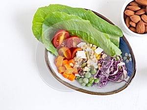 Mixed vegetable salad on oval plate and almond over white wooden background. Top view, with copy space