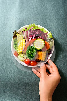 Mixed vegetables salad on white dish holding by hand