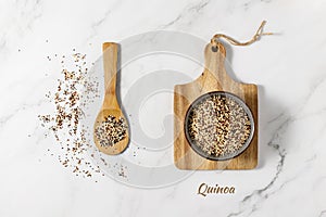 Mixed white, red and black quinoa grains on wooden spoon and in ceramic bowl. Raw seeds scattered on marble table