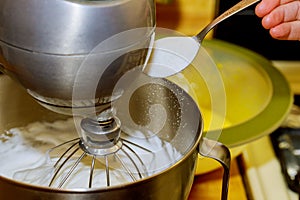 The mixer whipping egg whites. Woman adds sugar to mixer bowl