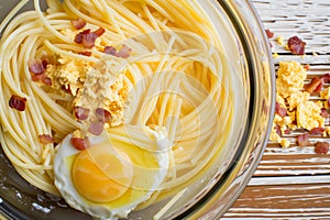 mixing bowl with whisked eggs next to a pile of spaghetti and bacon bits photo