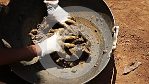 Mixing the clay inside a basket with gloves on hand from natural mud from a paddy farm for making some craft objects