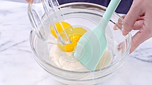 Mixing egg yolk into cake batter with green rubber spatula mixer tool stirring until smooth and blend well in a glass bowl, close