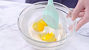 Mixing egg yolk into cake batter with green rubber spatula mixer tool stirring until smooth and blend well in a glass bowl, close