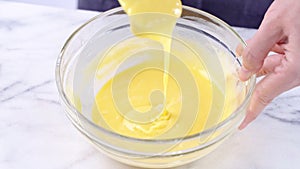 Mixing egg yolk into cake batter with green rubber spatula mixer tool stirring until smooth and blend well in a glass bowl, close