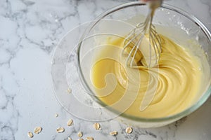 Mixing eggs, flour and milk in bowl with silver wire whisk. Concept of Cooking ingredients and method on white marble background,