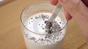 Mixing kefir or yogurt with chia seeds in a glass on a wooden cutting board.