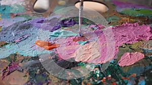 Mixing oil acrylic paints on a palette with a brush. Bright colored paint close up. Artist mixes paints on the palette