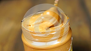 Mixing with a Spoon peanut butter. Creamy smooth peanut butter in jar backdrop