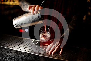 Mixologist pouring sweet juicy cocktail into a glass on bar