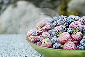 A mixt of frozen strawberries, blackberries, raspberries covered with hoarfrost on a plate on a gray background. Close