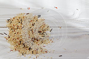 A mixture of brown, wild, red, white rice lies on a slide on the wooden white surface of the table