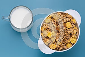 A mixture of cereals dried and nuts with milk at breakfast. Glass cup of milk with rolled oats in a white plate on blue table. Whi