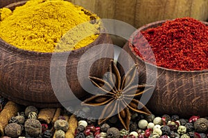 A mixture of colorful aromatic peppers, star anise, paprika and turmeric in a wooden bowl in close-up