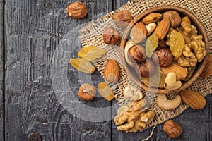A mixture of dried fruits and nuts in a wooden bowl on a piece of burlap on a wooden table. Flat lay
