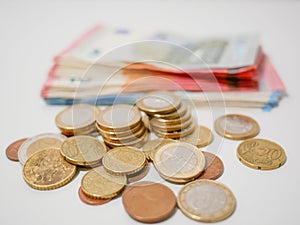 Mixture of Euro coins and banknotes lying on a white desk. Notes and coins of various denominations.