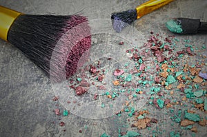 A mixture of eye shadows and applicators crumbled on a rustic steel table. Confusing jumble of cosmetic products photo