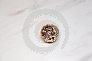 Mixture of peppers hot, red, black, white and green pepper seasoning in a wooden bowl, top view