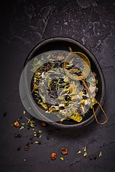 Mixture of teas, dried organic tea herbs and fruits in bowl with tea strainer