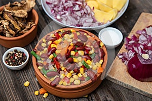 Mixture of vegetables, dried boletus mushrooms, sliced potato, red onion sliced and whole on a cutting board and spices