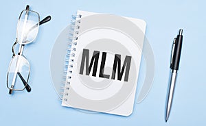 mlm words in white notepad, pen and glasses on blue background. Concept