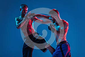 MMA. Two professional fighters punching or boxing isolated on blue studio background in neon