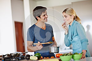 Mmm, my tastebuds are doing the happy dance. a handsome young man giving his wife a taste of his cooking.