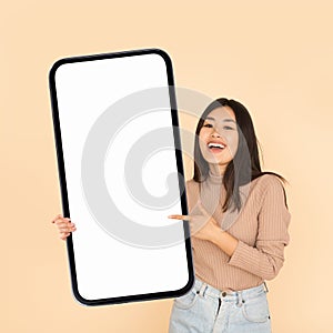 Mobile Ad. Smiling Asian Woman Holding And Pointing At Big Blank Smartphone