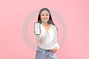 Mobile app ad. Happy asian lady showing white empty smartphone screen, recommending application or website, mockup