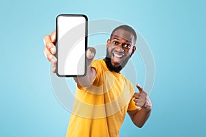 Mobile app advertisement. Excited black man pointing at smartphone with empty screen, mockup. Space for ad or website