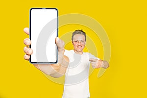 Mobile app advertising handsome blond man pointing at giant smartphone with white empty screen, wearing white t-shirt