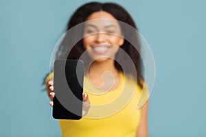Mobile app concept. Happy african american woman showing smartphone with blank screen over blue background