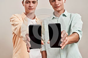 Mobile app. Two young caucasian twin brothers in casual wear showing smartphone with blank screen while standing