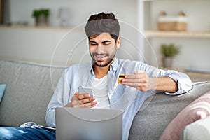 Mobile banking concept. Positive arab guy using smartphone and credit card for online shopping