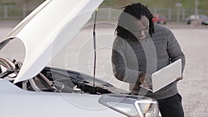 Mobile car assistance. African american black man running diagnostic on broken car on his laptop