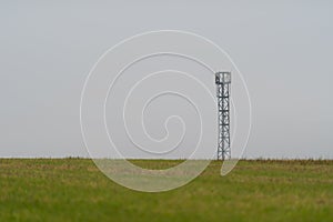 Mobile cell tower antenna mast providing mobile internet connection for rural area standing on empty barren field on grey overcast