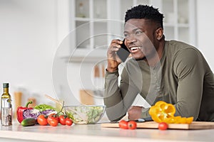 Mobile communication. Happy handsome black man talking on cellphone in kitchen