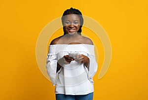 Mobile Communication. Portrait Of Happy Young Black Woman Holding Smartphone, Yellow Background